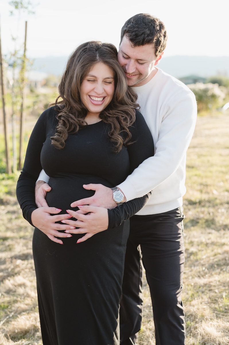 pregnant women in black and the man has a white sweater and he's hugging her bump by Photographer Jen Vazquez