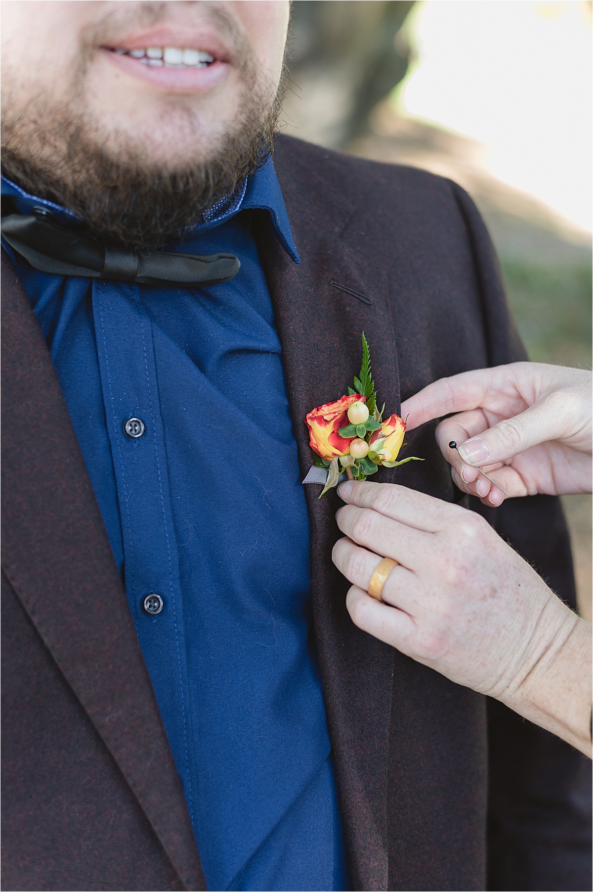 groom getting a boutonniere put on in a blue shirt with brown suit