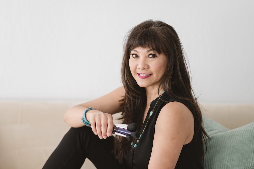 Monina Wright of Moderne Beauty holding makeup sitting on a couch in black