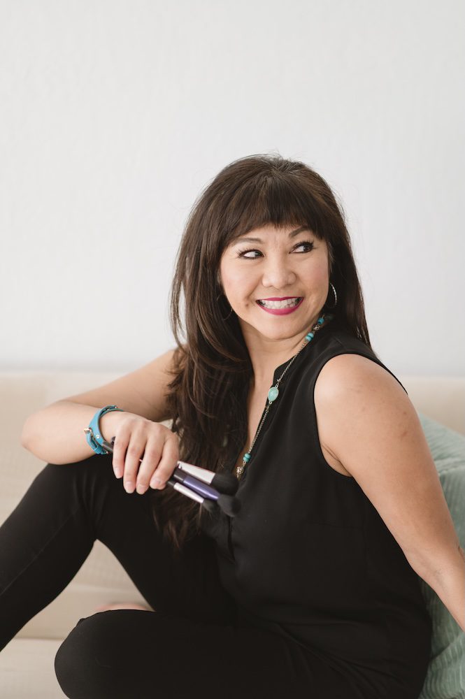 Monina Wright of Moderne Beauty holding makeup sitting on a couch in black