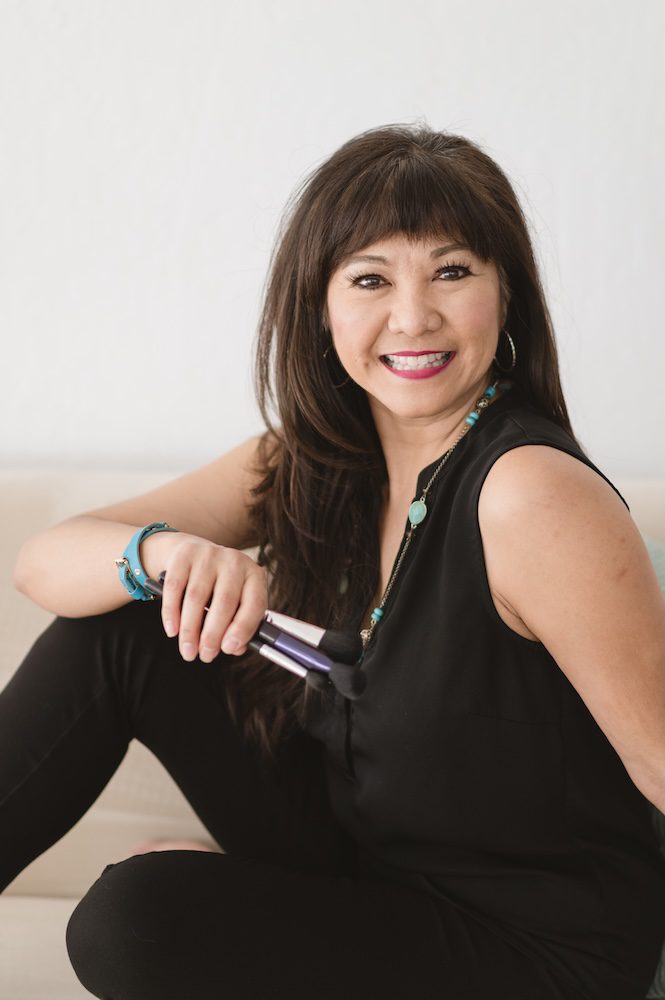 Monina Wright of Moderne Beauty holding makeup sitting on a couch in black