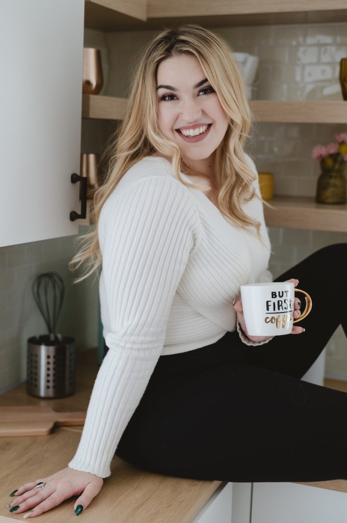 girls sitting on a kitchen counter with a cup of coffee in a white sweater and black leggings