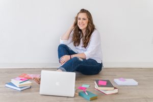 Female service provider sitting on the floor surrounded by her laptop, many books, and a notebook and pen