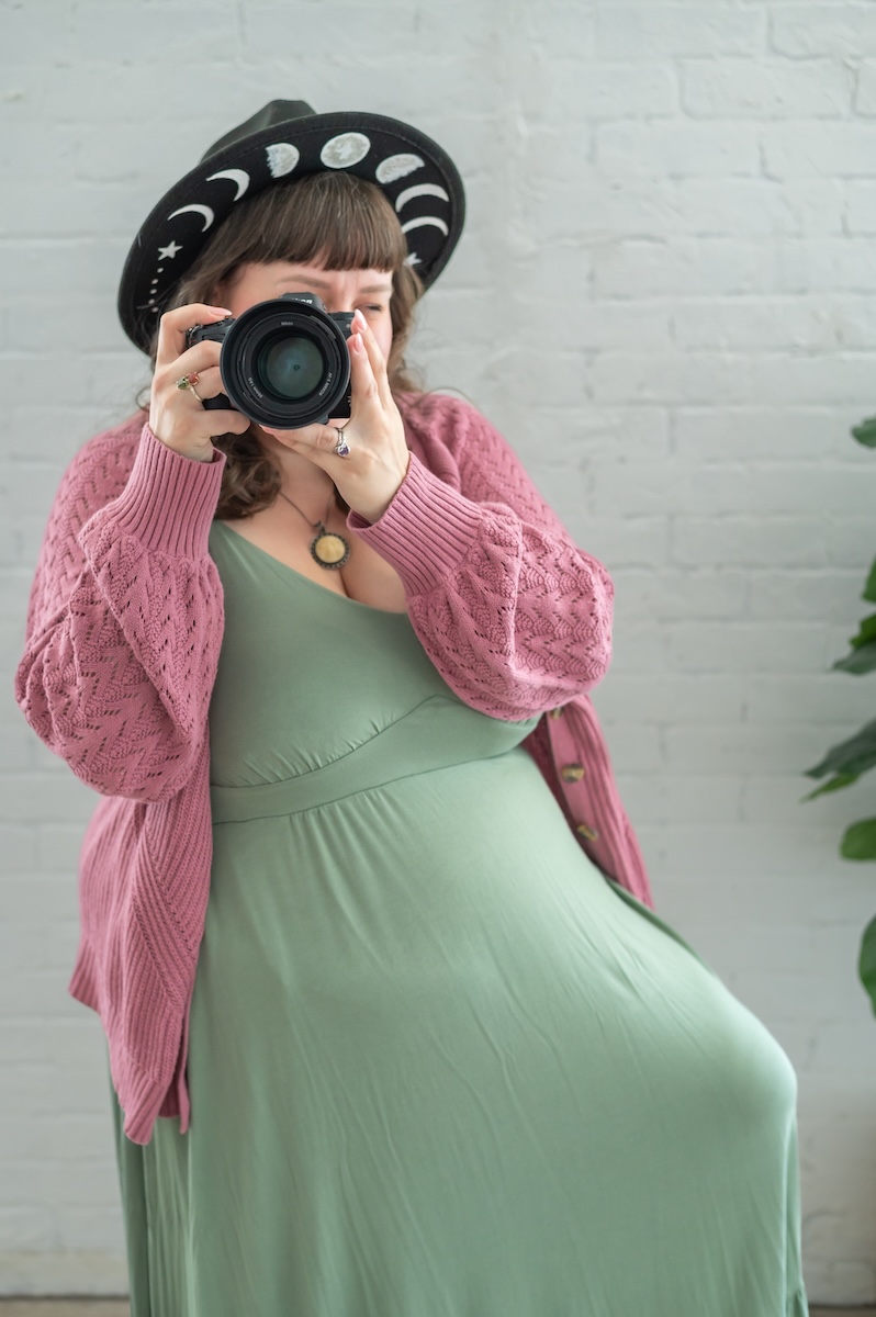 newborn photographer and business coach with green dress and pink mauve sweater holding her nikon Z6ii mirrorless camera for a photoshoot with Jen Vazquez in the Bay Area of Northern California