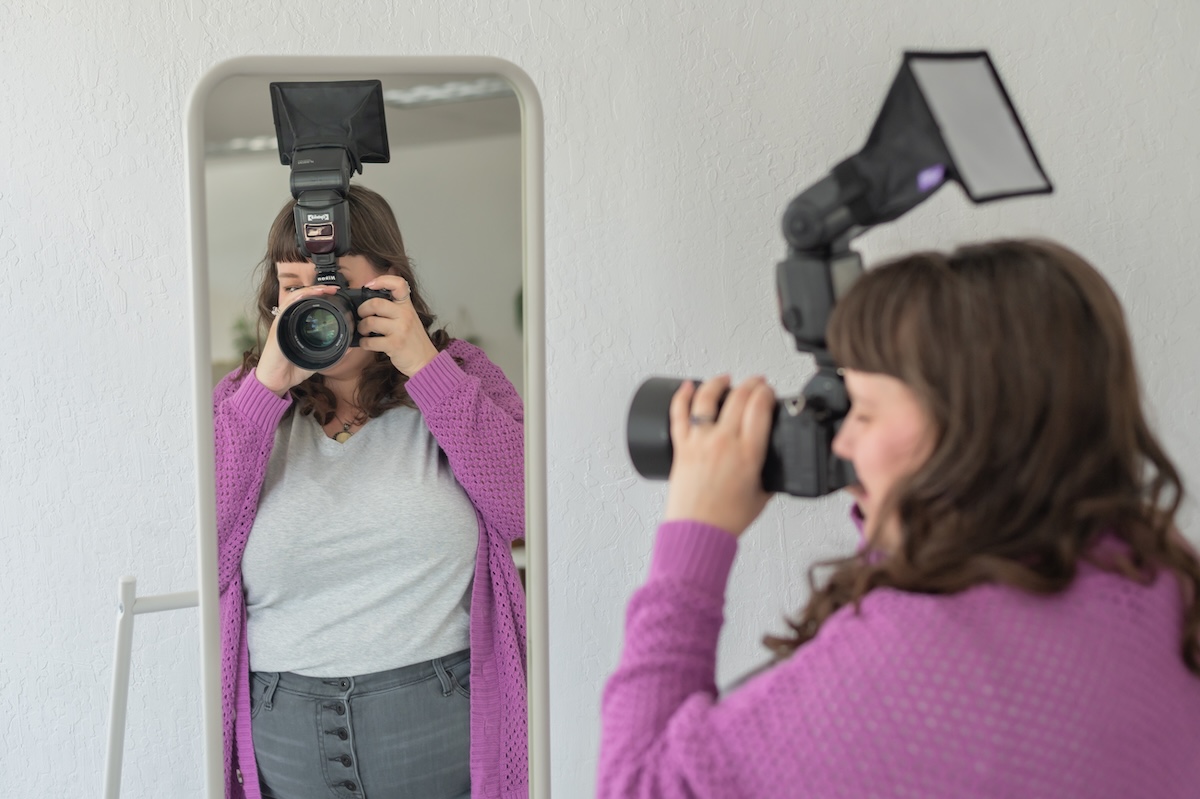 Photographer with her camera in a white shirt with purple sweat and gray jeans with a black hat being photographed by Jen Vazquez Media in the Bay Area of Northern California San Jose