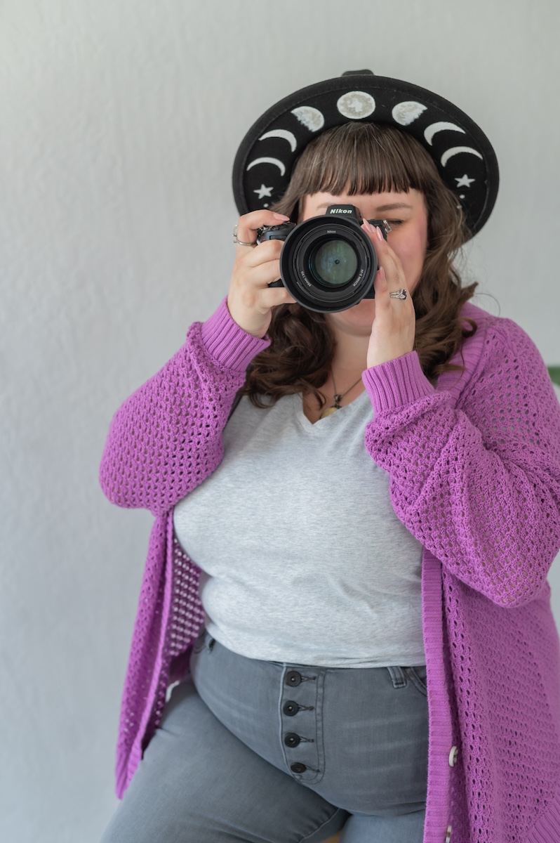 Photographer with her camera in a white shirt with purple sweat and gray jeans with a black hat being photographed by Jen Vazquez Media in the Bay Area of Northern California San Jose