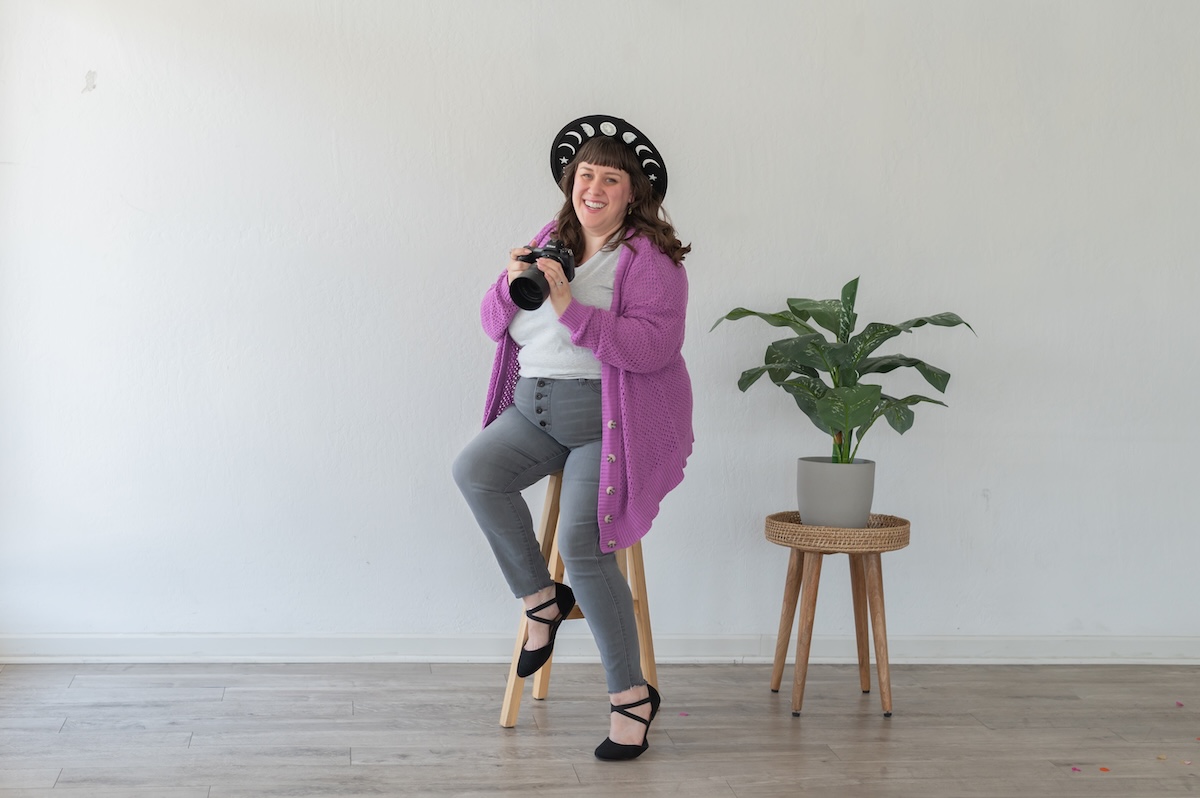 Photographer with her camera in a white shirt with purple sweat and gray jeans with a black hat being photographed by Jen Vazquez Media in the Bay Area of Northern California San Jose