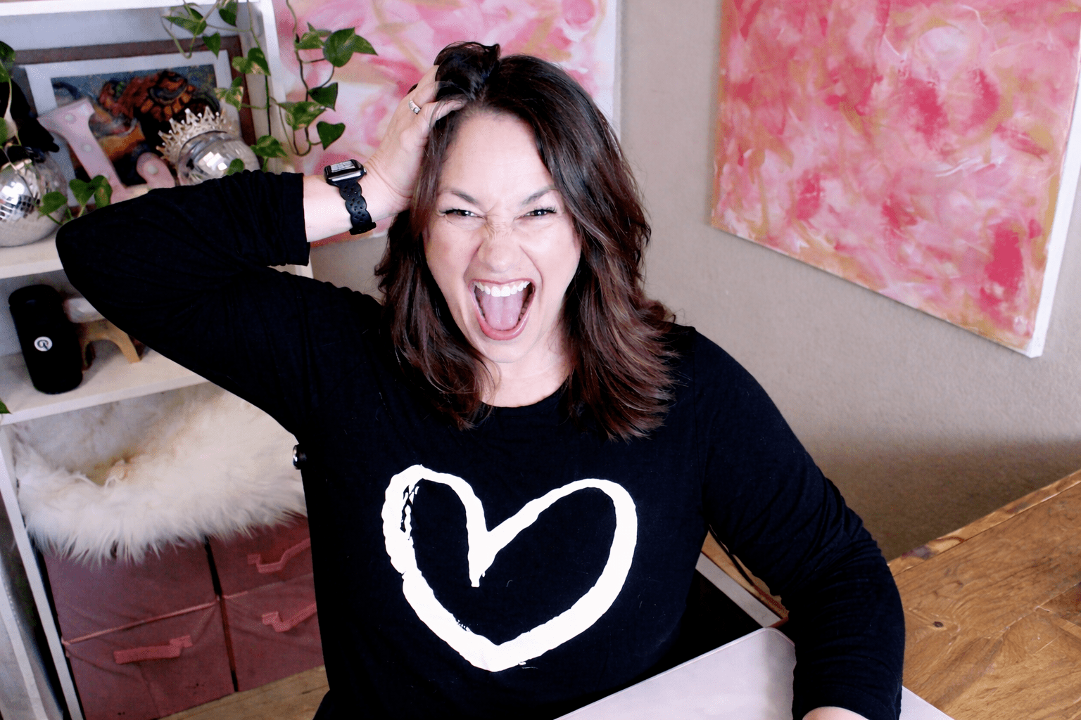 Jen Vazquez looking overwhelmed sitting at her desk in a black shirt with a white heart on it